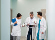 Trois médecins échangent dans le couloir d'un établissement de santé lors d'une garde médicale, illustrant la coordination des équipes et la continuité des soins.