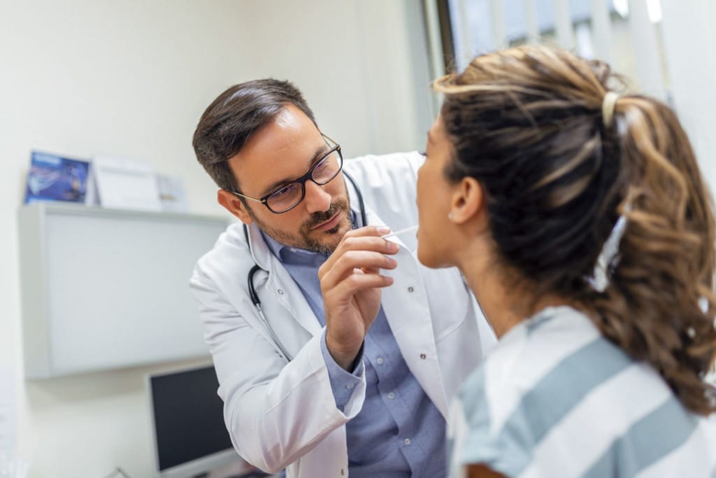 Médecin ORL réalisant un examen de la gorge d'une patiente lors d'une consultation médicale en cabinet.