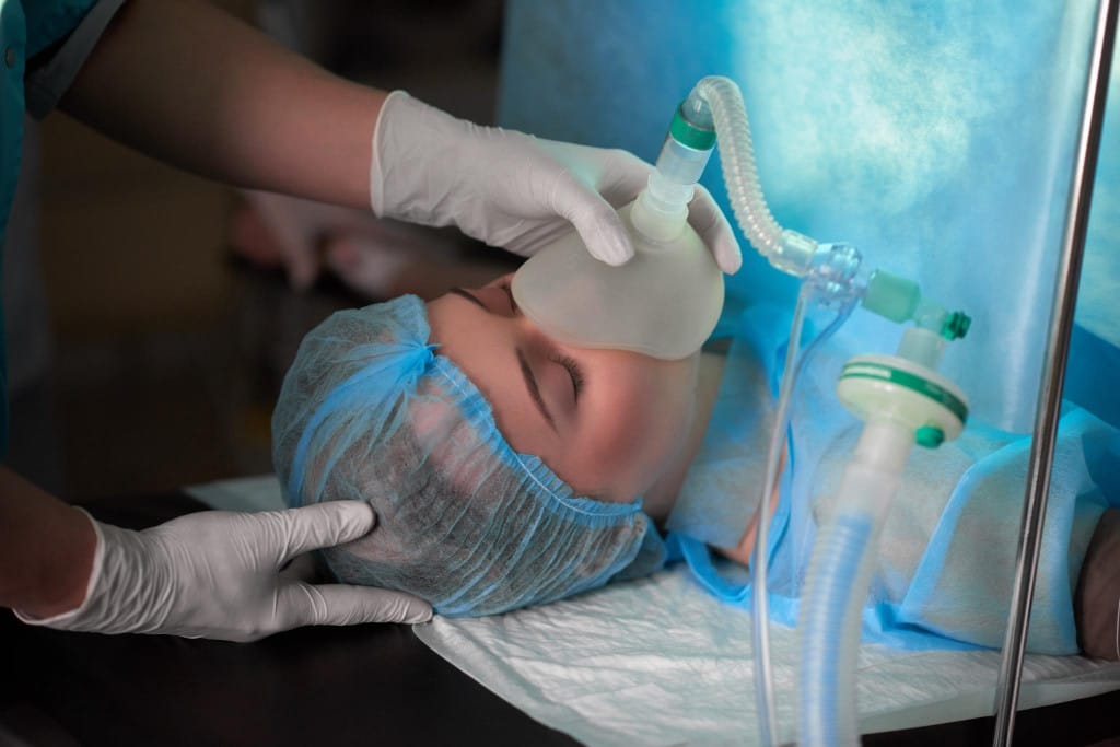 Patiente sous anesthésie générale portant un masque respiratoire avant une intervention chirurgicale au bloc opératoire.